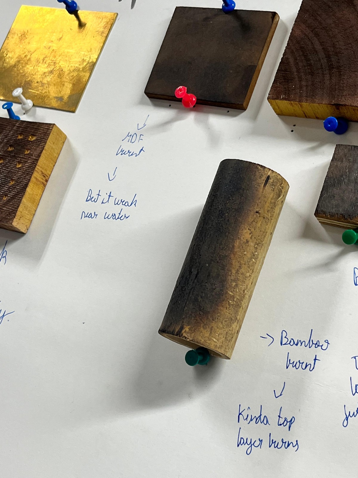 Burnt wood samples pinned to the board with handwritten notes: MDF weak near water, bamboo only the top layer burns