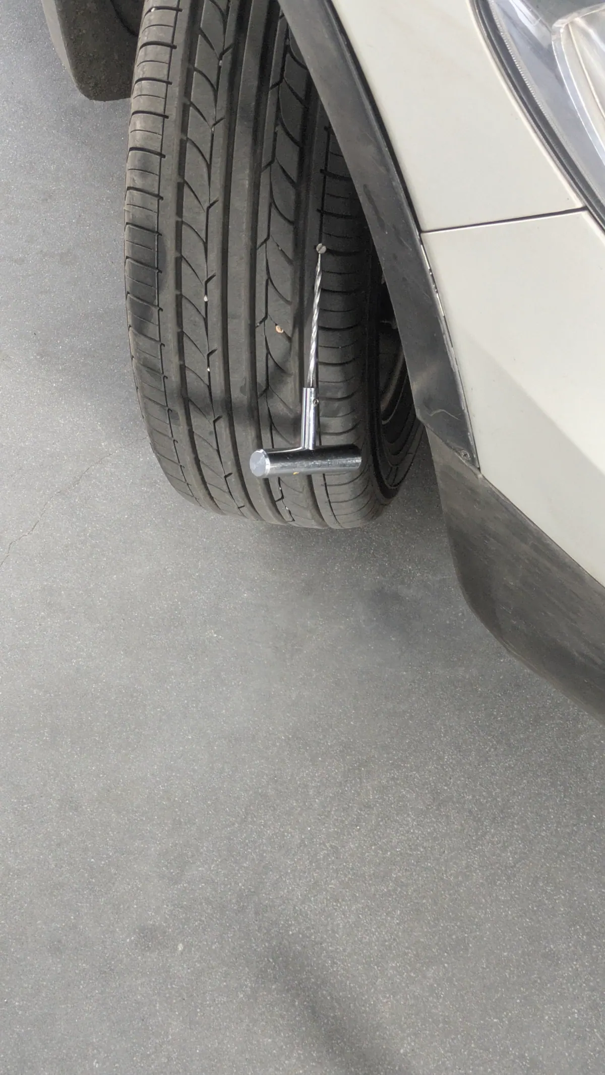 A T-handle spiral reamer pushed into the tread of a front tyre, the wheel still on the car